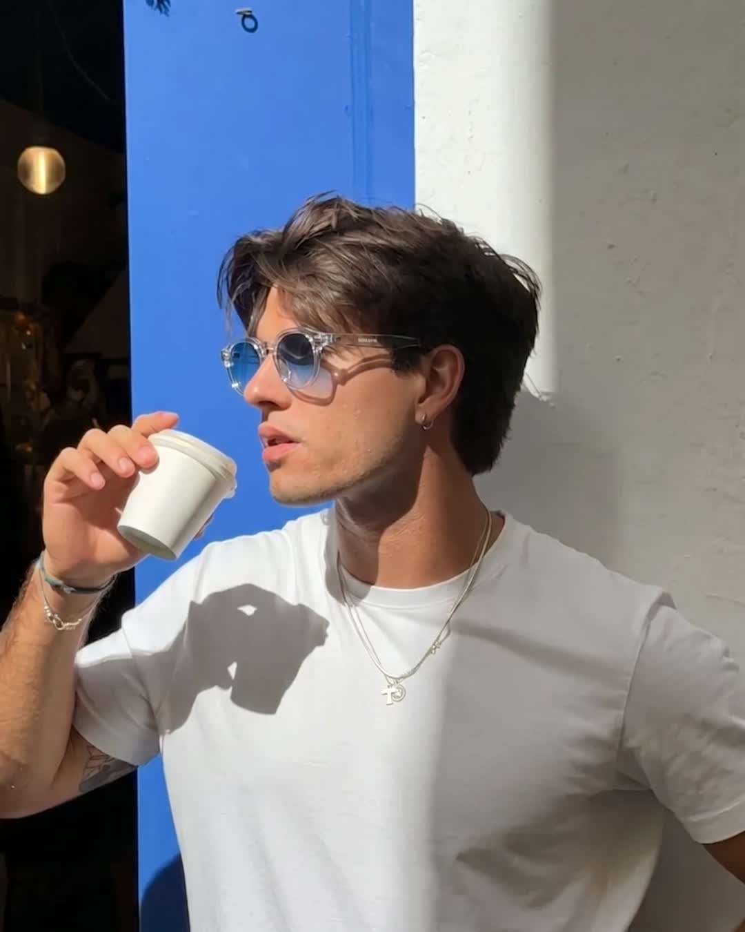 Man wearing Aura Eyes blue-tinted round sunglasses against a blue wall